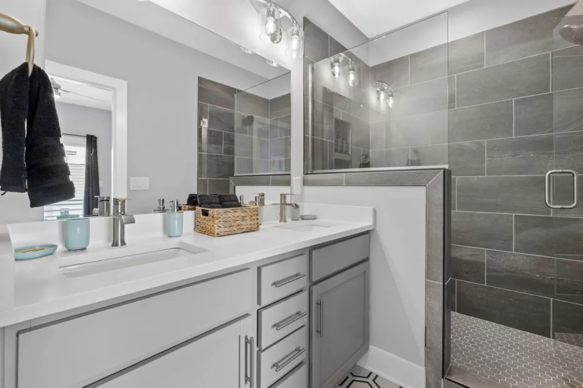 A modern bathroom with a double sink vanity, expansive mirrored wall, and a spacious shower area. The decor is bright and calming, promising a spa-like experience.