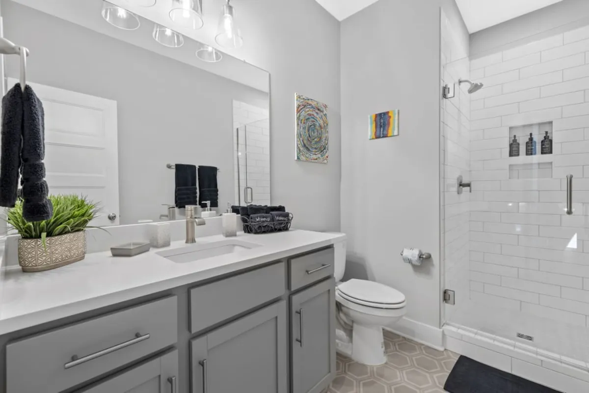A bright and inviting laundry area with double sinks, a large mirror, shower enclosure, and colorful artwork. The space feels well-equipped and clean, perfect for guests seeking comfort and convenience during their stay.