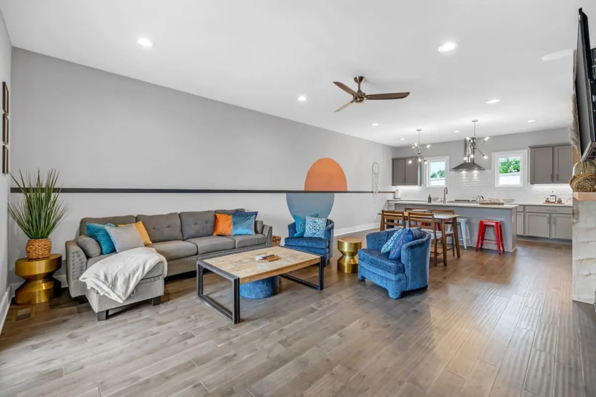 An open-concept living area with a plush sofa, coffee table, blue accent chairs, and a kitchen island in view. The space is bright and casual, tailored for both relaxing and entertaining—a natural extension of the living area for hosting or unwinding.