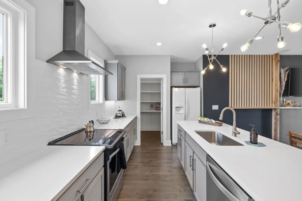 A sleek, modern kitchen featuring stainless steel appliances, white countertops, modern lighting, and welcoming wooden accents. The scene is lively, hinting at both cooking and socializing, and suggests a space equipped for both casual breakfasts and festive feasts.