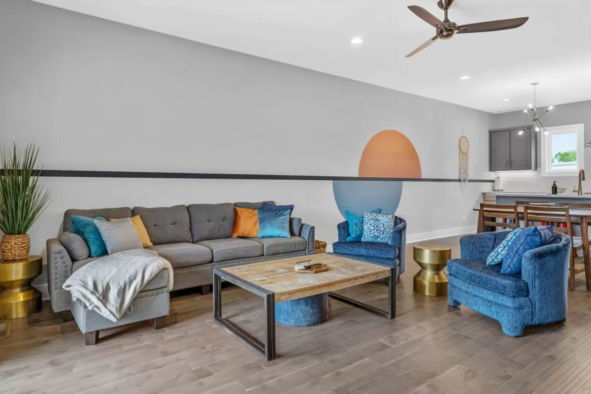 A bright, inviting living area with a sofa, accent chairs, coffee table, and wall art. Large windows suggest a connection to the outdoors, and the mood is comfortable and inviting, ideal for gathering and enjoying the flow between interior and exterior spaces.
