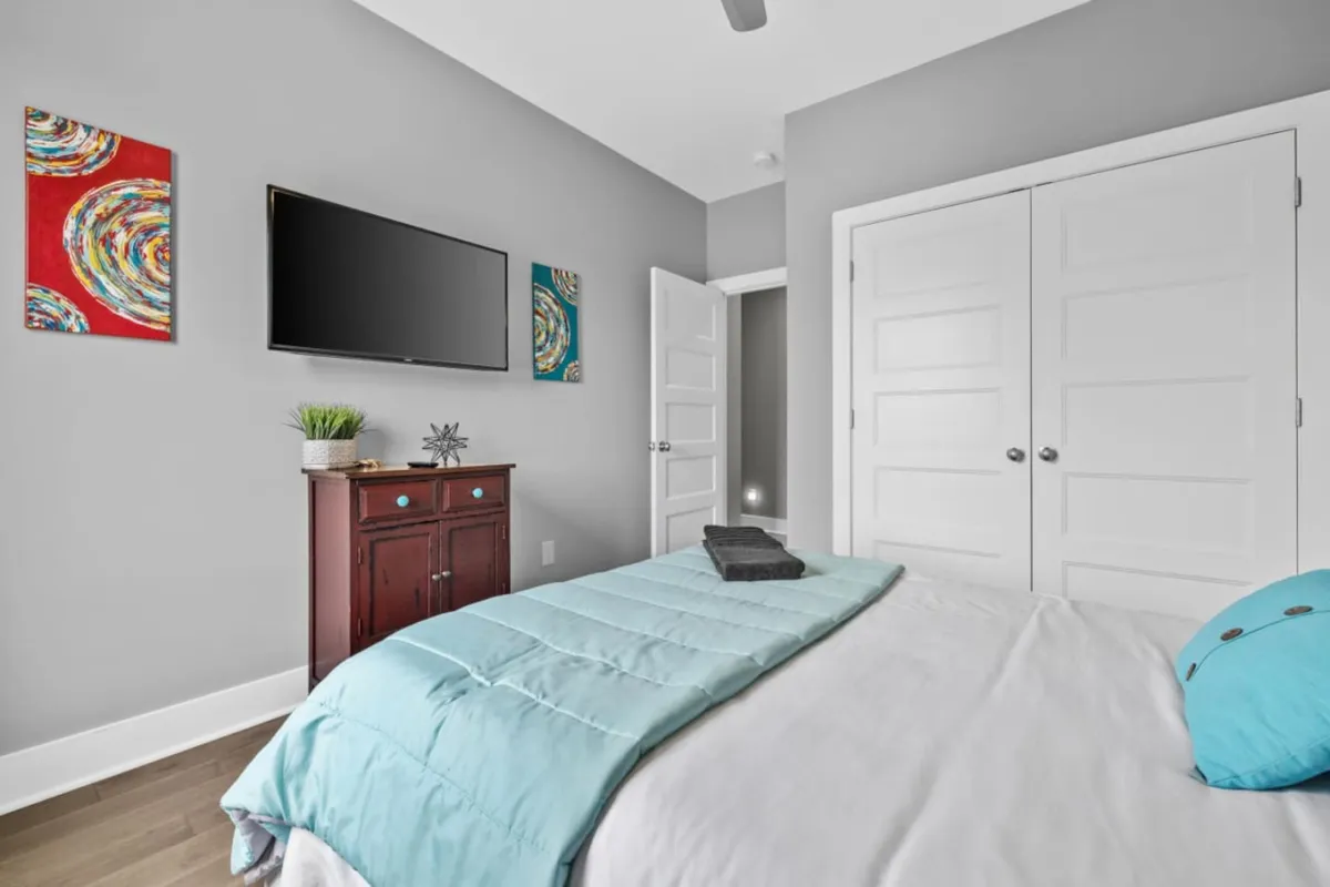 A comfortable bedroom with teal bedding, modern wall art, a television, and a nightstand. The space offers a serene atmosphere suitable for relaxing, watching TV, or reading before bed, highlighting a private retreat for winding down after a day of adventures.