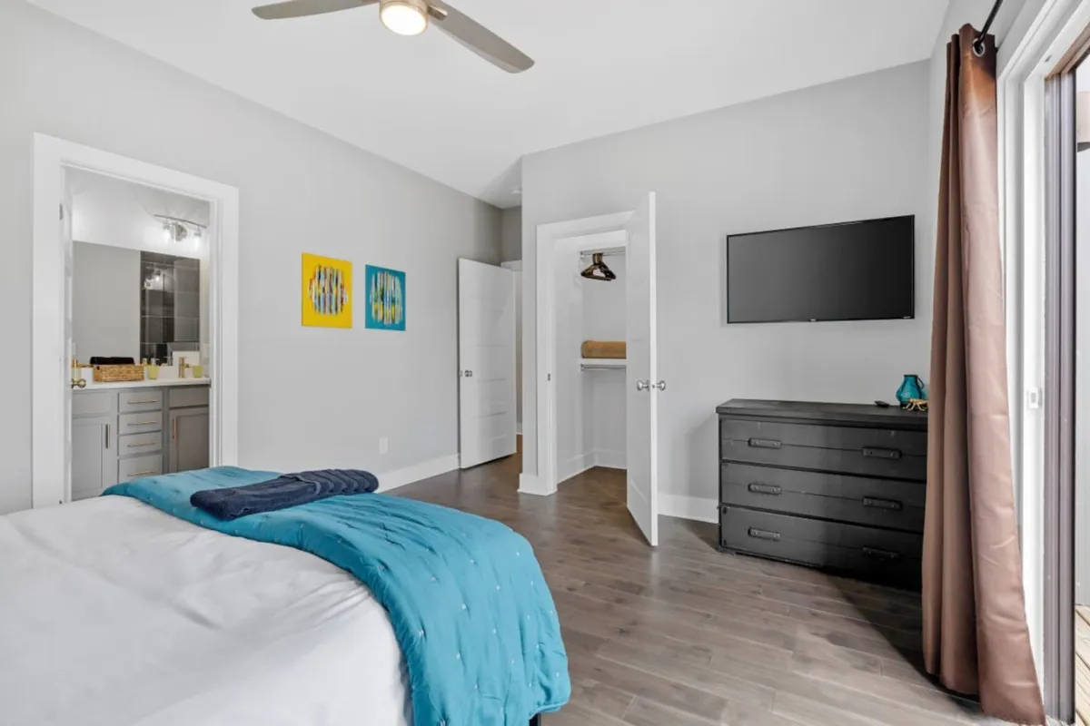 A cozy bedroom featuring a full bed with a teal cover, a black dresser, a wall-mounted TV, and unique wall art. The space feels inviting and tailored for relaxation or entertainment.