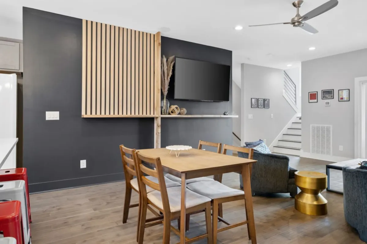 The image showcases a warm, contemporary living and dining area with a wooden slat wall, a dining table designed for group meals or game nights, a large television ideal for watching shows or sports, and decorative elements that add personality and comfort. The layout invites gatherings and highlights the social heart of the home.
