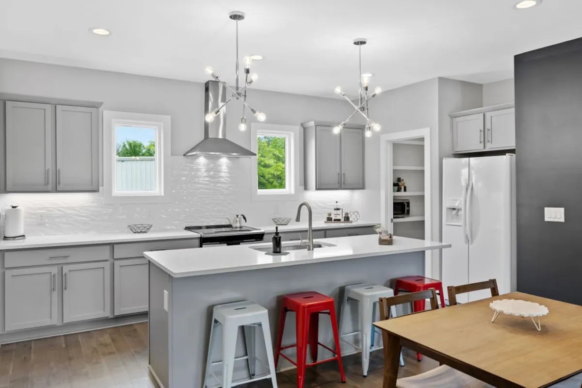 A welcoming, contemporary kitchen and dining area featuring a central island with stools, a chandelier overhead, and a large dining table set for socializing. The space is designed for group gatherings and entertaining, with warm lighting and stylish finishes.