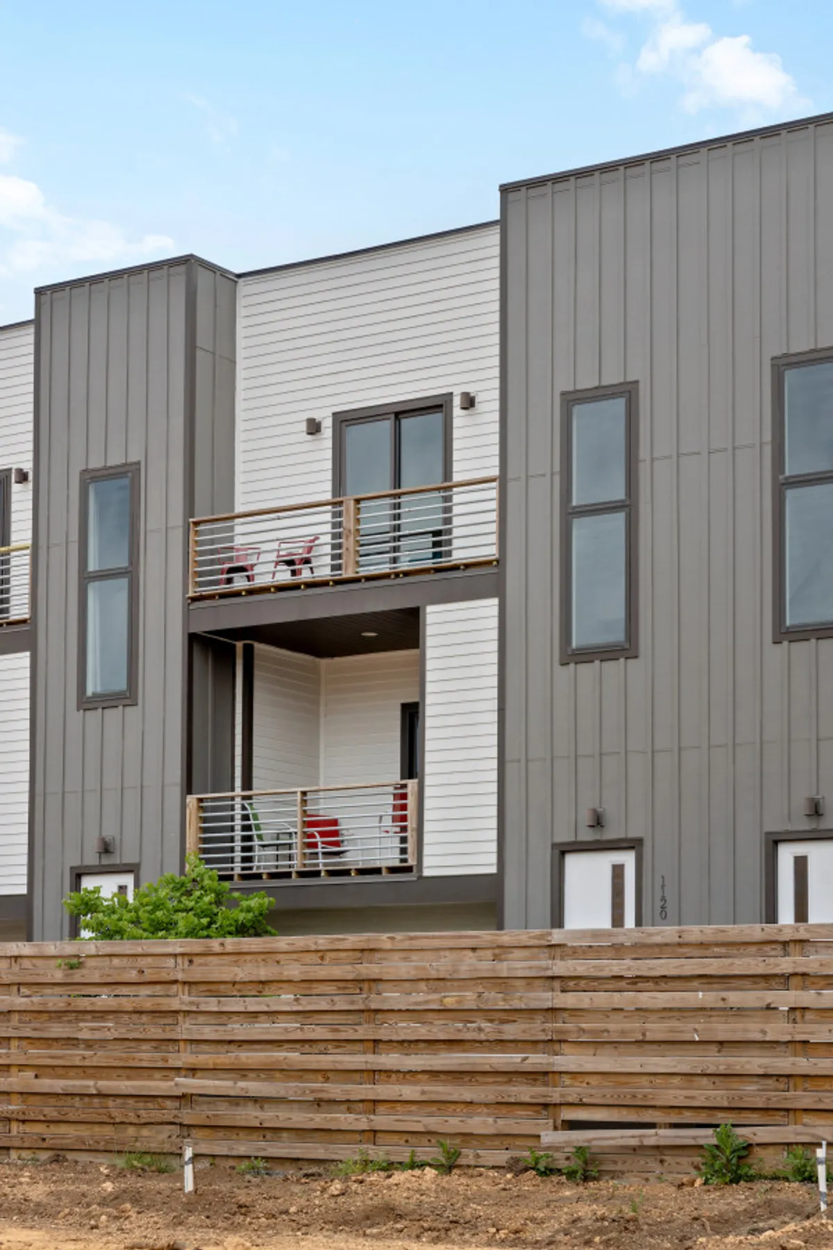 A contemporary balcony with comfortable seating and a stylish wooden fence, set against modern architecture. The setup is perfect for relaxing, sipping a drink, or sharing stories while enjoying the outdoors—the ideal spot for al fresco dining or evening gatherings.
